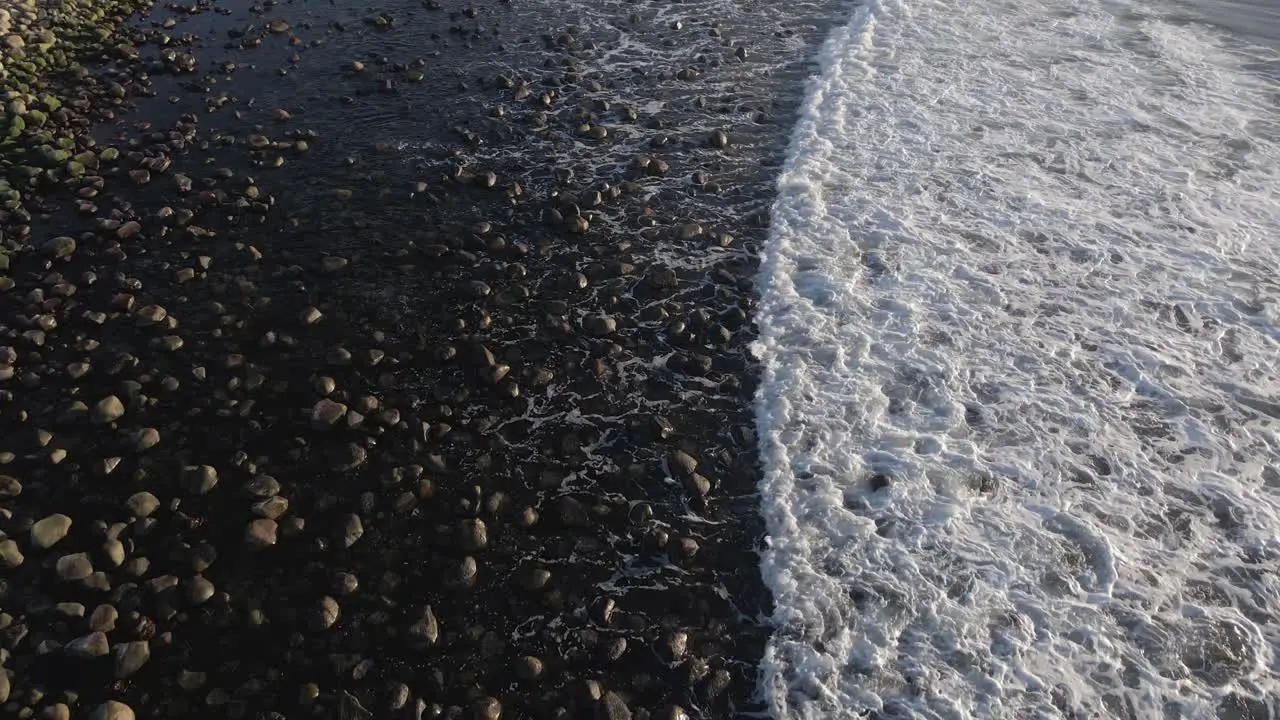 Ocean waves roll over sandy and rocky coastal beach aerial view