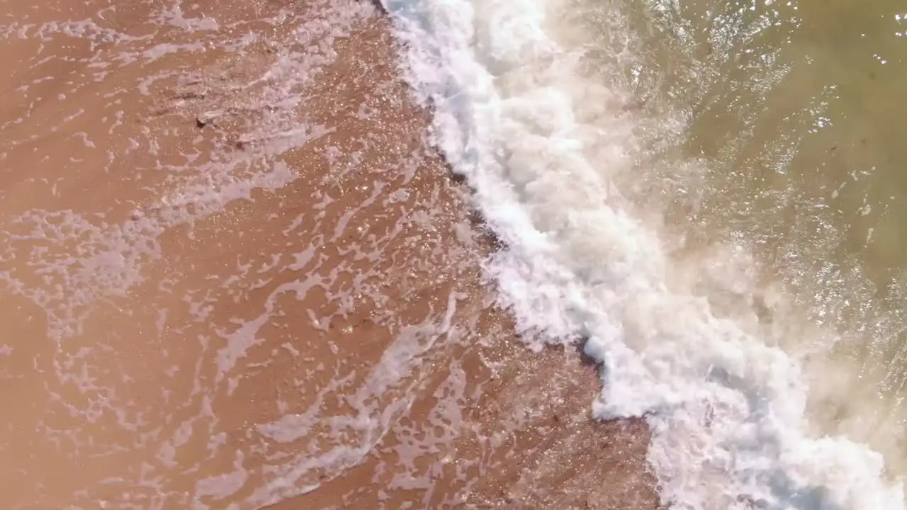 Overhead aerial of waves foam splashing against shore spiral zoom in day