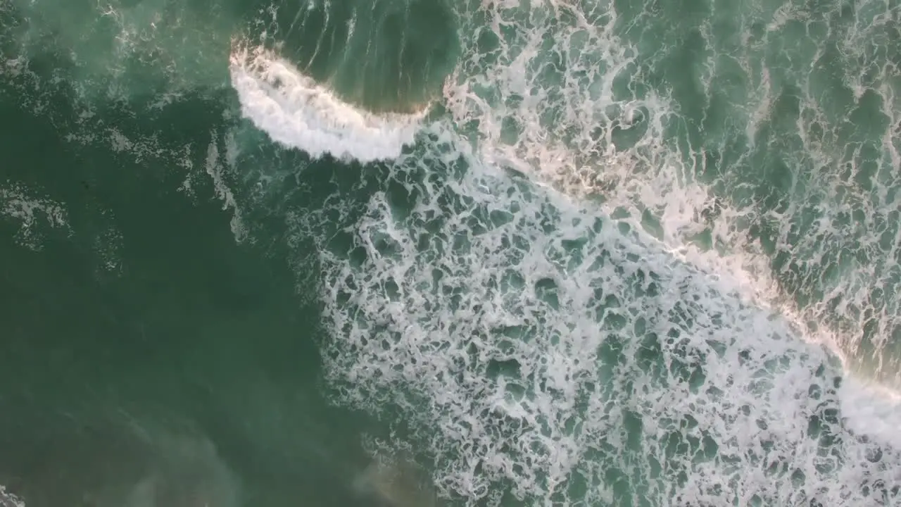 An aerial perspective looking straight down at the ocean with waves rolling in 2