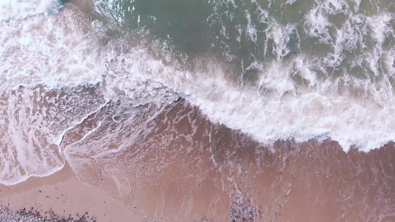 Static aerial looking down at fast waves crashing on a pink sand beach