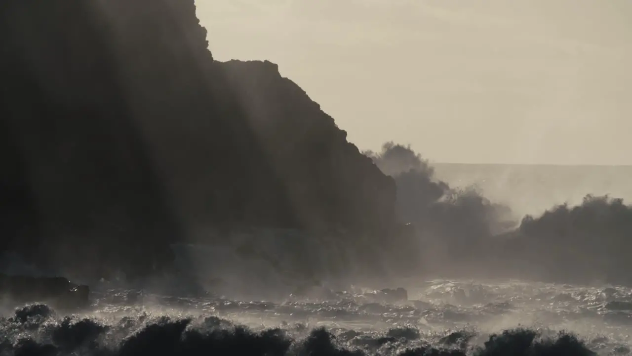 Blue waves roll into the coast of Hawaii and crash into the shore in slow motion during a big storm