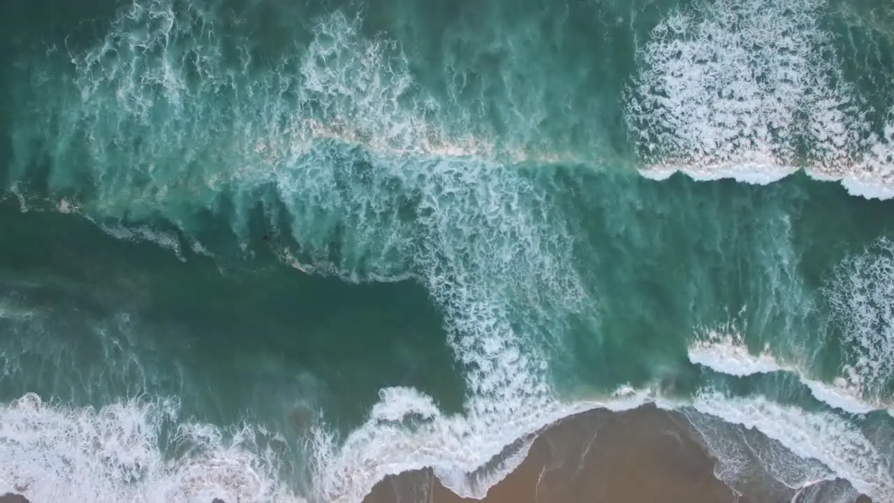 An aerial perspective looking straight down at the ocean with waves rolling in