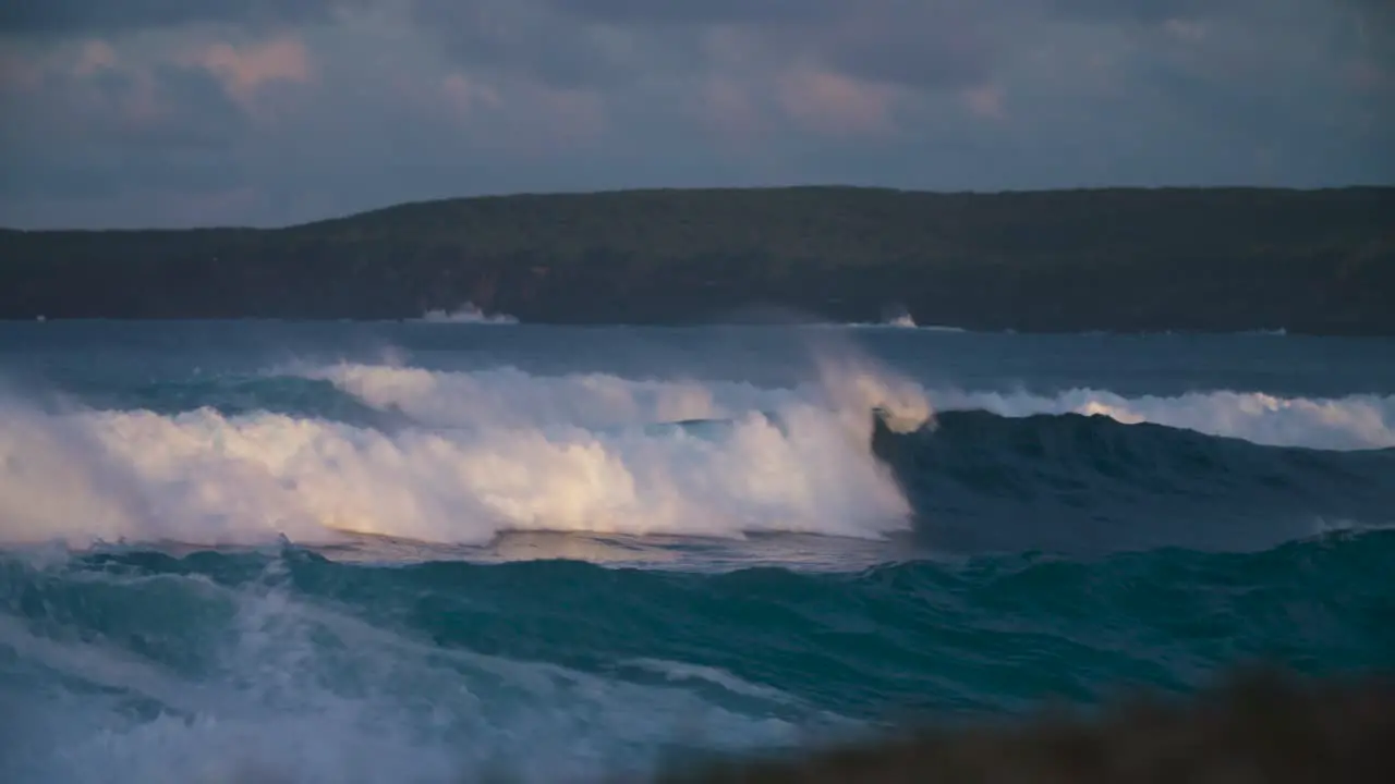 Ocean waves roll into a coastline in golden light in slow motion