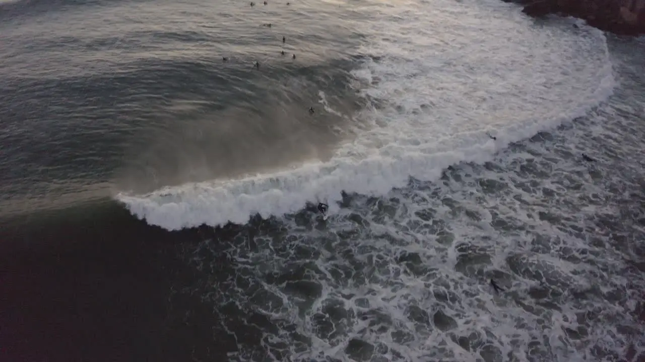 Aerial drone view of some surfers riding some waves in almost night on coast of Portugal