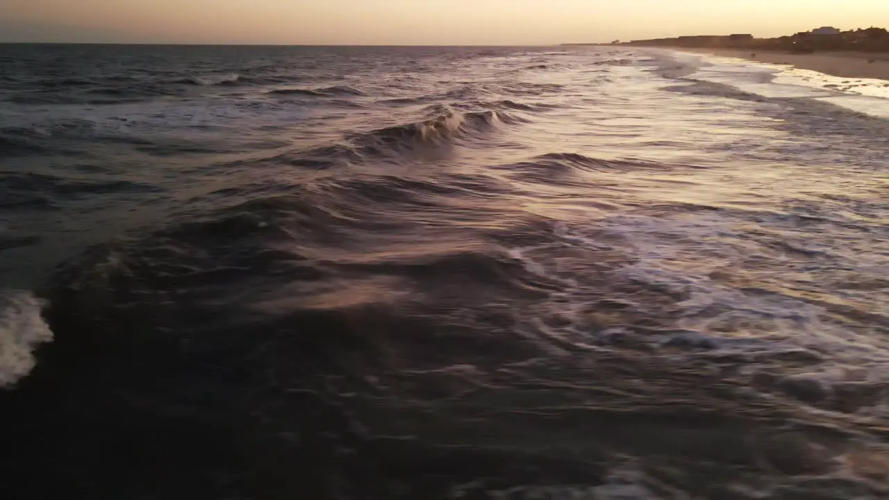 Fast drone shot at beach during warm sunset of waves rolling in