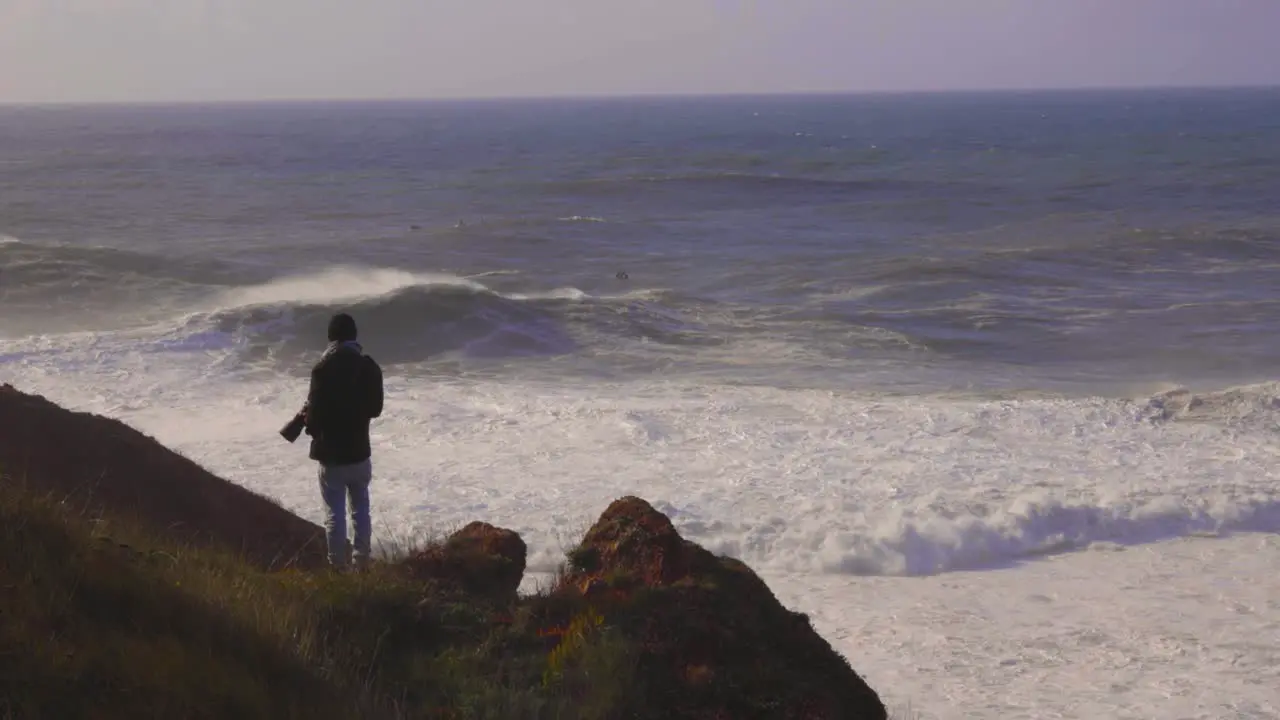 Photographer on top of a cliff with big waves in the background