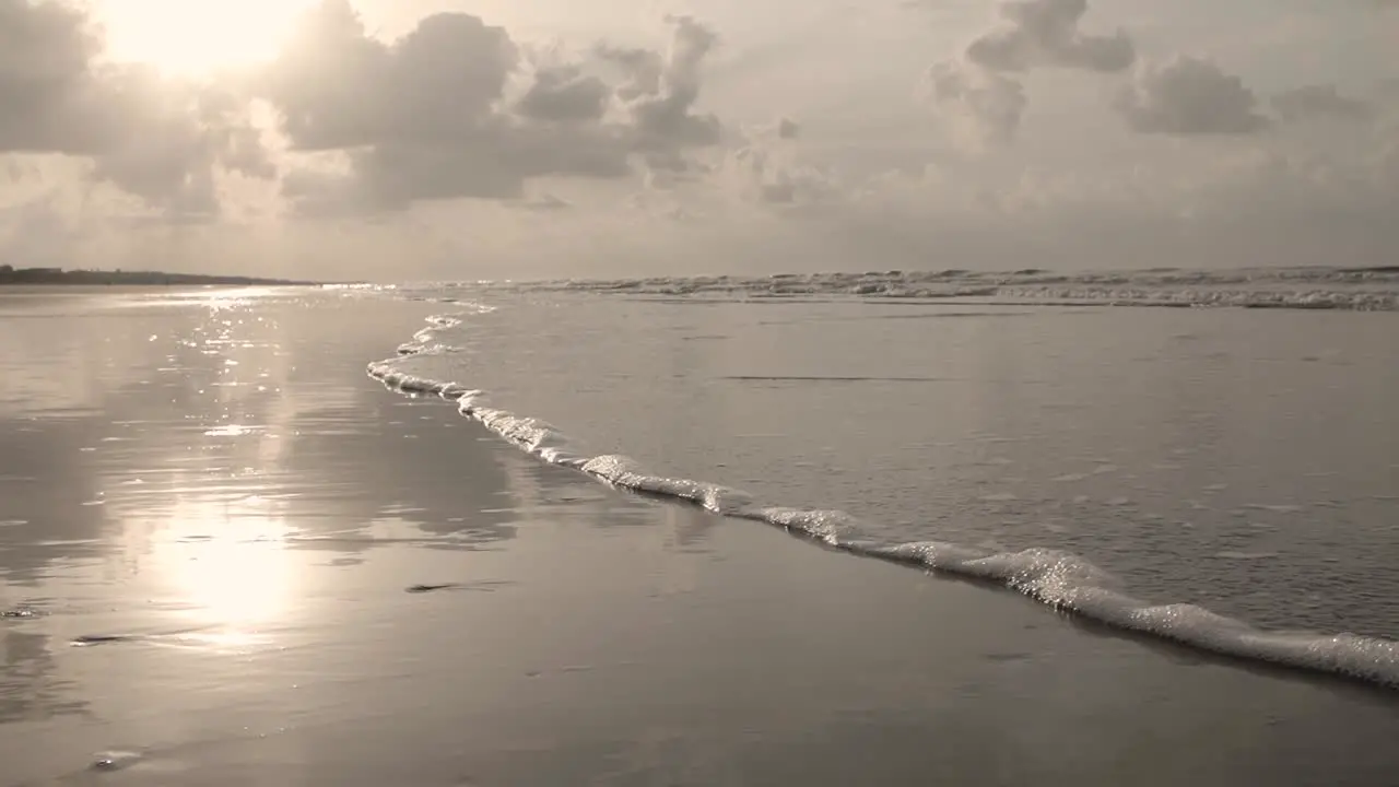 Slow motion close up low angle of water lapping on beach at sunrise