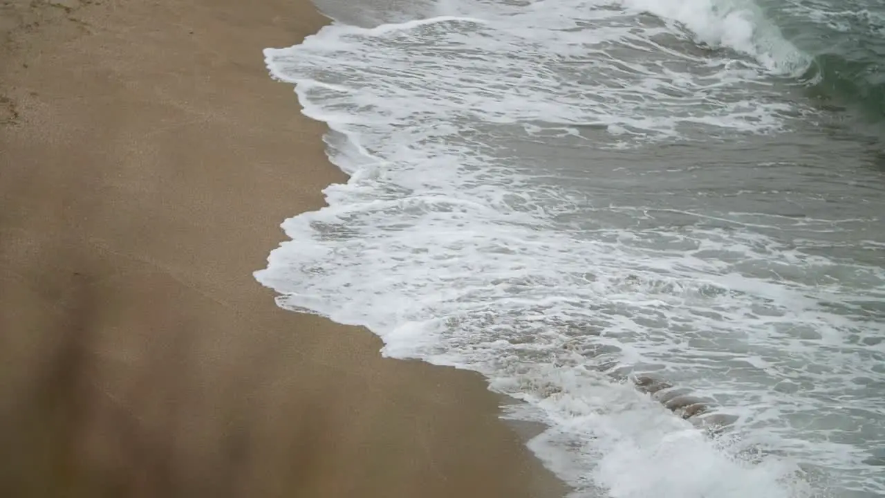 Side view of waves deepening the sand shot in slow motion with tele lens from a higher point of view