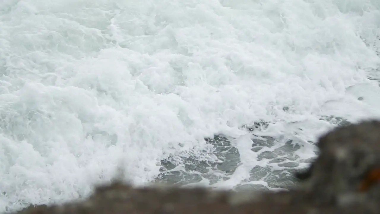 Slow motion wave foam in tight shot with rock in the foreground