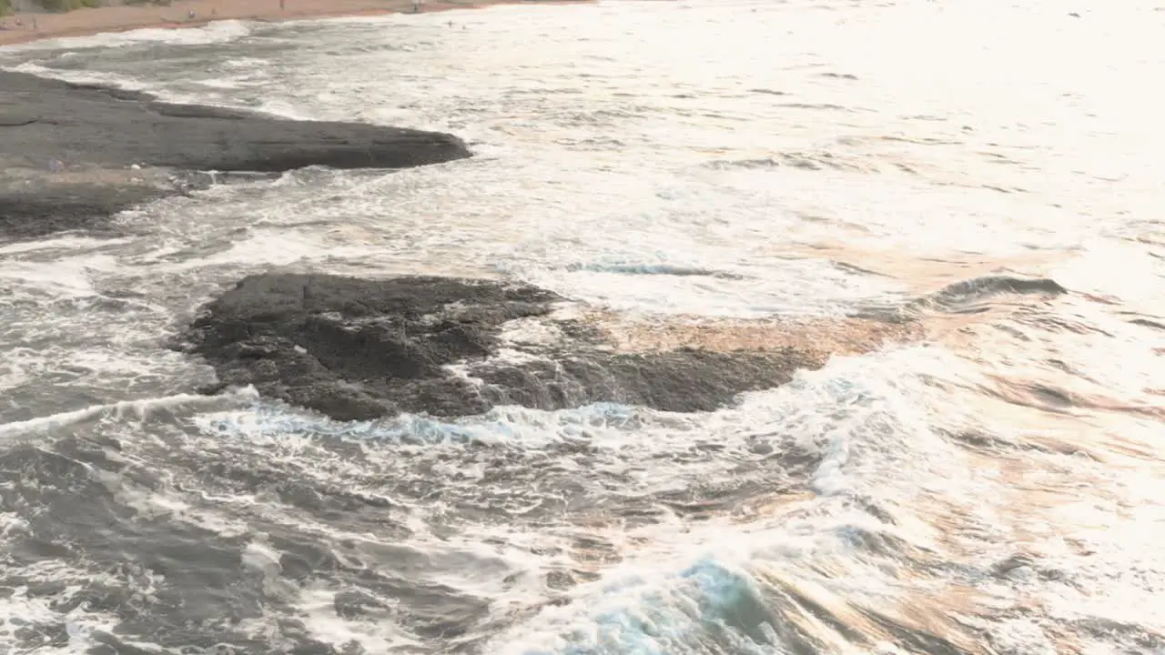 Drone slow motion footage of rock in the sea close to the seashore waves wash over the cliff