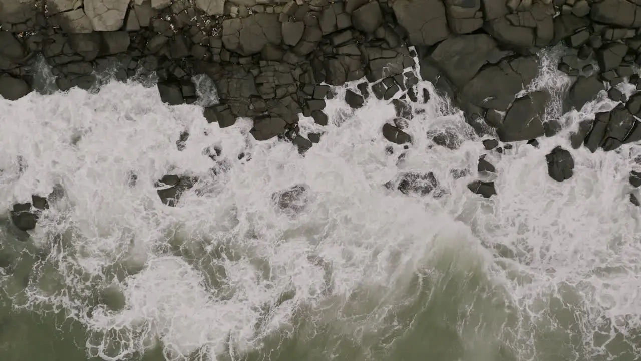 Wide slow motion aerial footage top down of ocean waves crashing into rocks