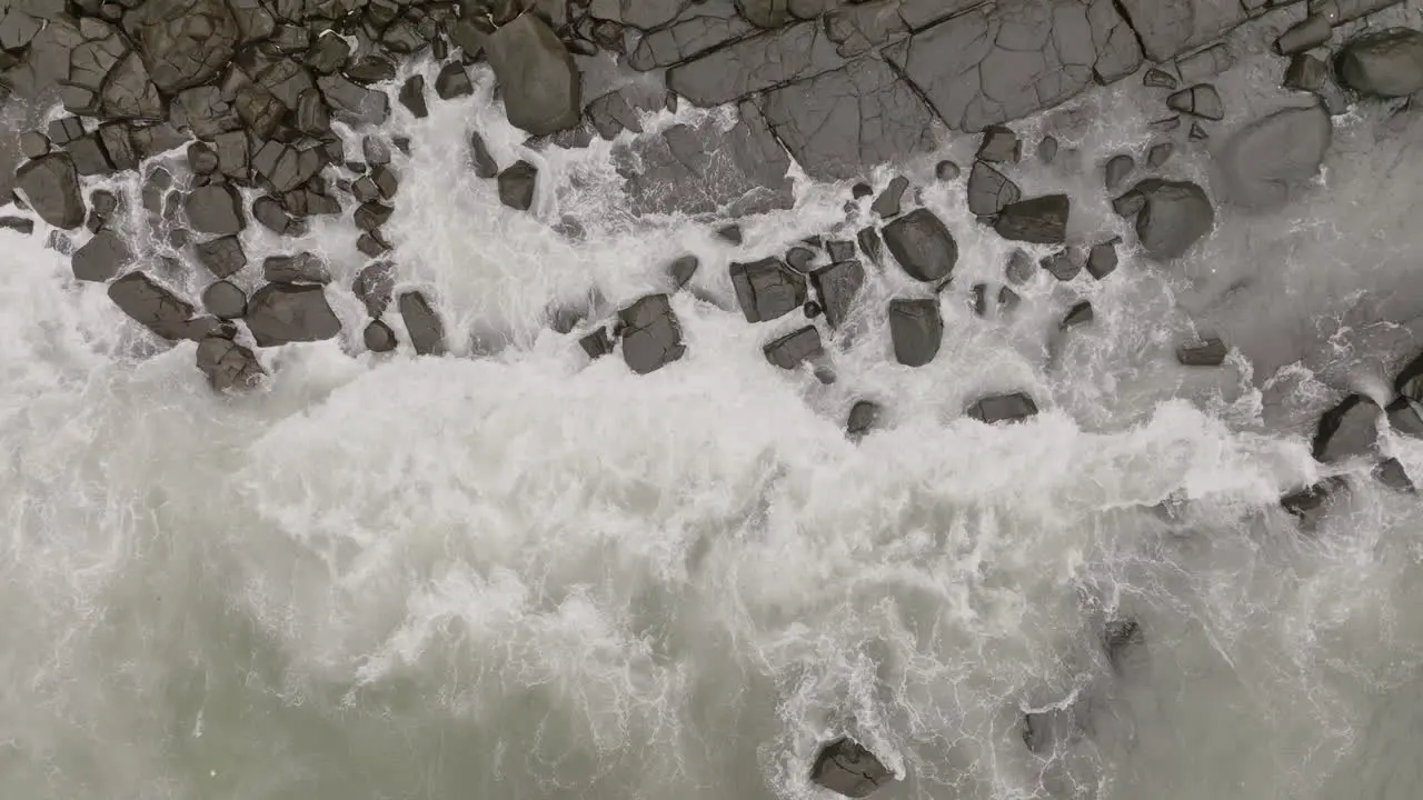 Close aerial footage top down of ocean waves crashing into rocks