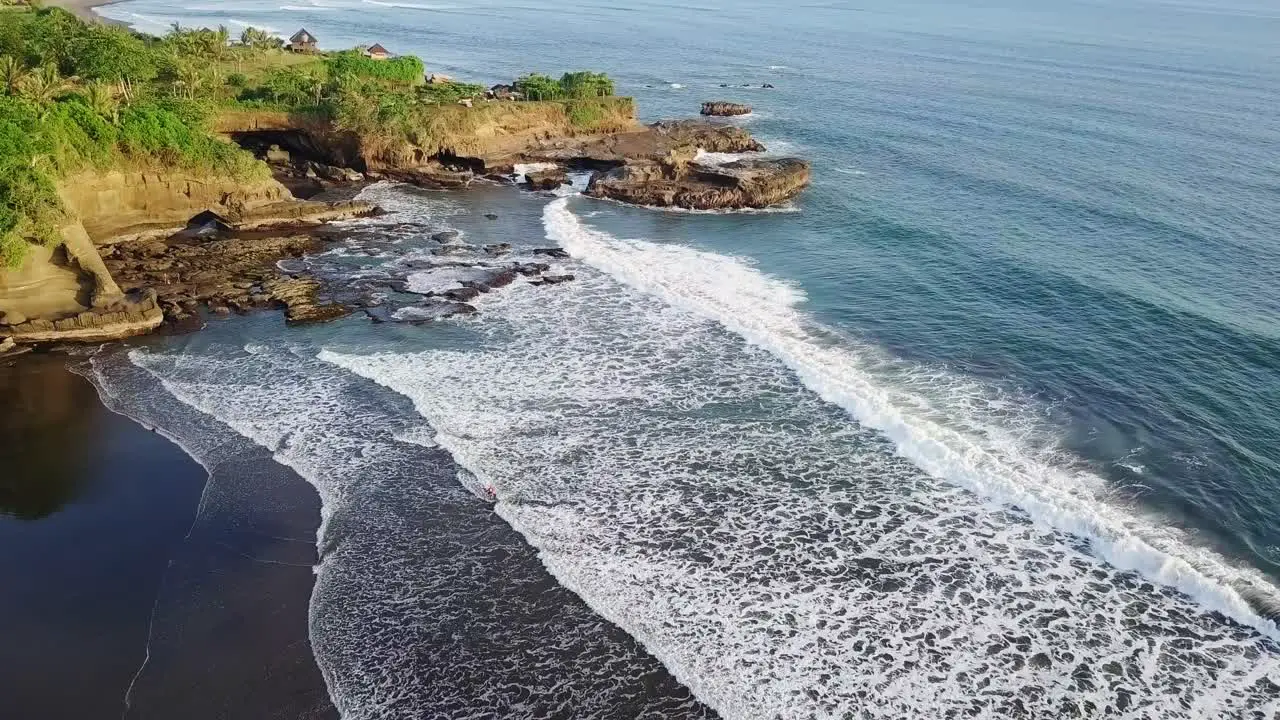 Aerial View Of A Beach With Waves Reaching The Shore And Green Cliff