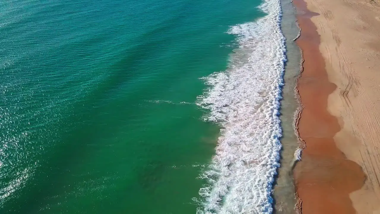 Aerial shot of long waves breaking into a empty sandy beach