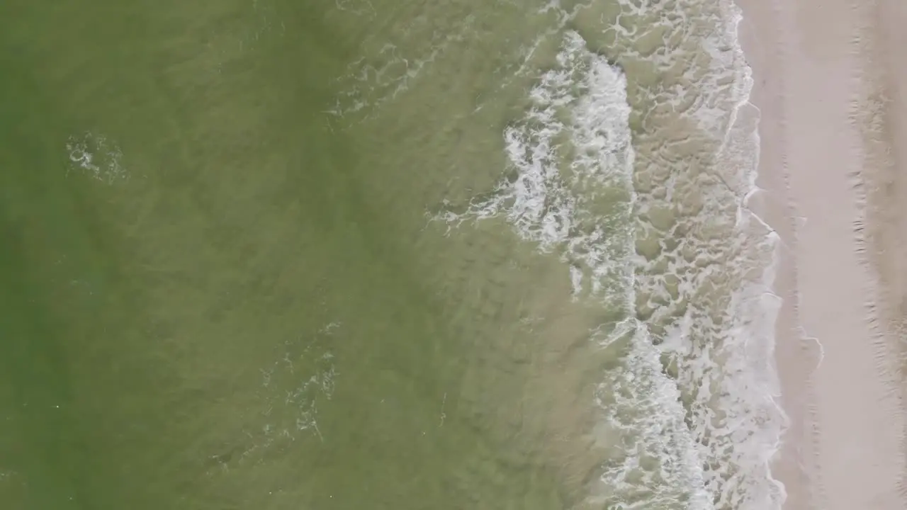 Aerial vertical shot of ocean waves rolling onto a sand beach