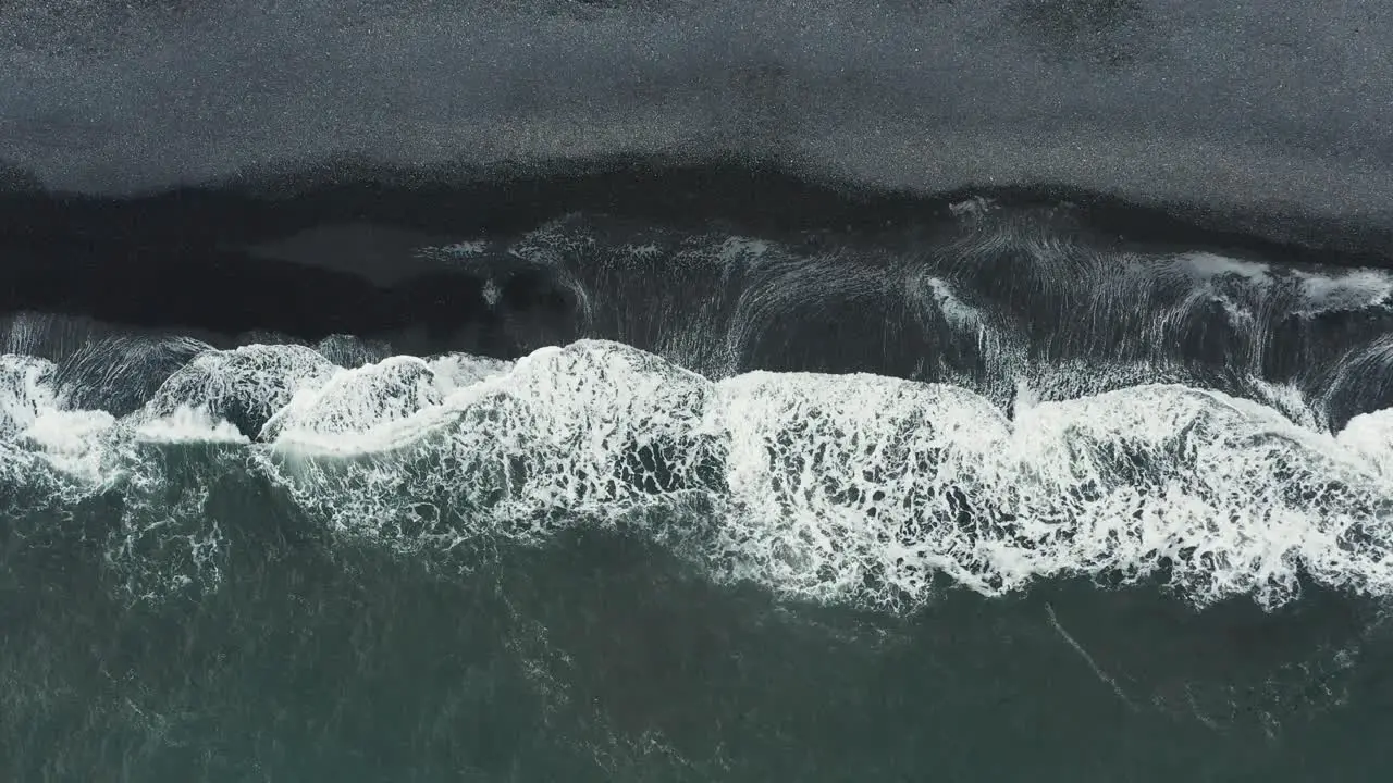 Waves rolling onto shore of black sand beach in Iceland aerial