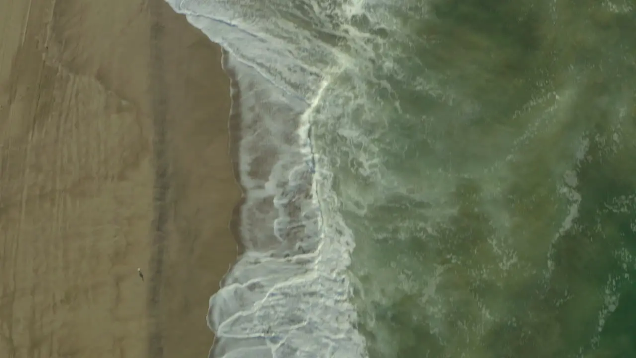 Aerial dolly shot looking down on the waves crashing on the sandy beach