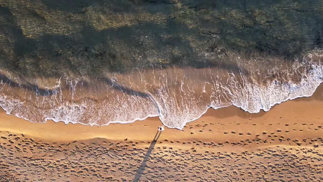 Top down aerial view of waves crushing on an empty beach with one man standing in the middle