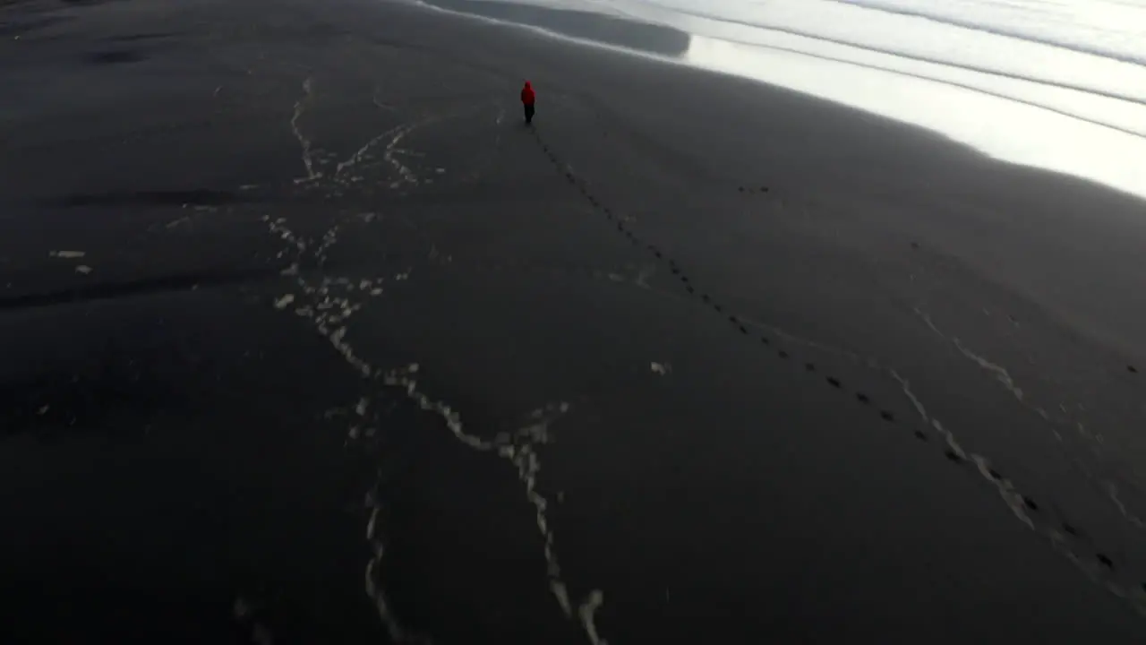 Drone footage of man on stokkness beach panning up towards dramatic mountains on the coast of southern Iceland