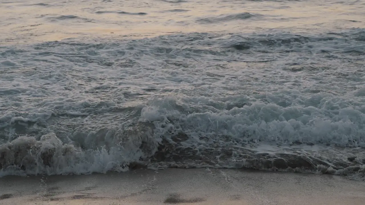 Huge waves from the wild Pacific Ocean roll onto the sandy beach as several people swim in the sea just after sunset in Mexico