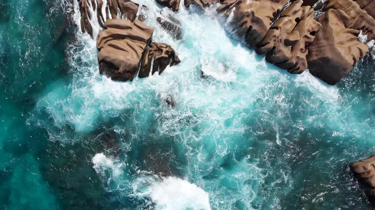 Zoom out aerial view of waves breaking on the granite rocks of Anse Marron on La Digues south tip