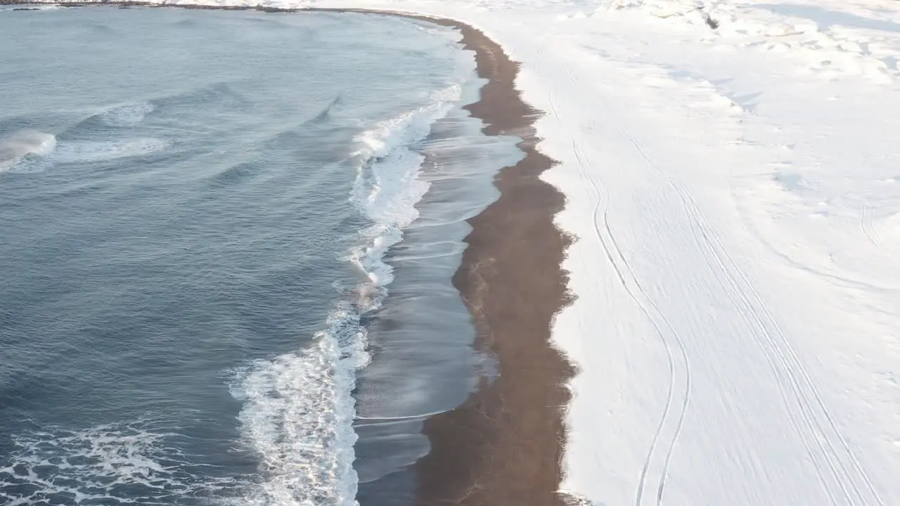 Snowy coastline at Sandvik beach in Iceland with waves aerial