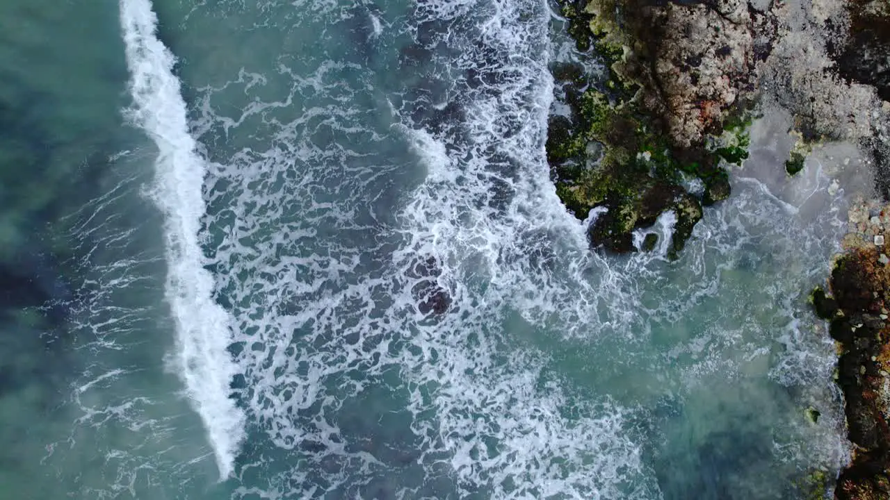 Top down drone view of turquoise waves breaking on rocky shore