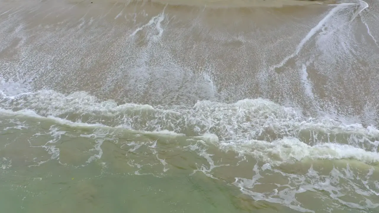 The camera captures the beauty of a tropical beach from above slowly moving down to showcase the striking contrast of the white foam and turquoise water as the waves crash onto the sandy shore