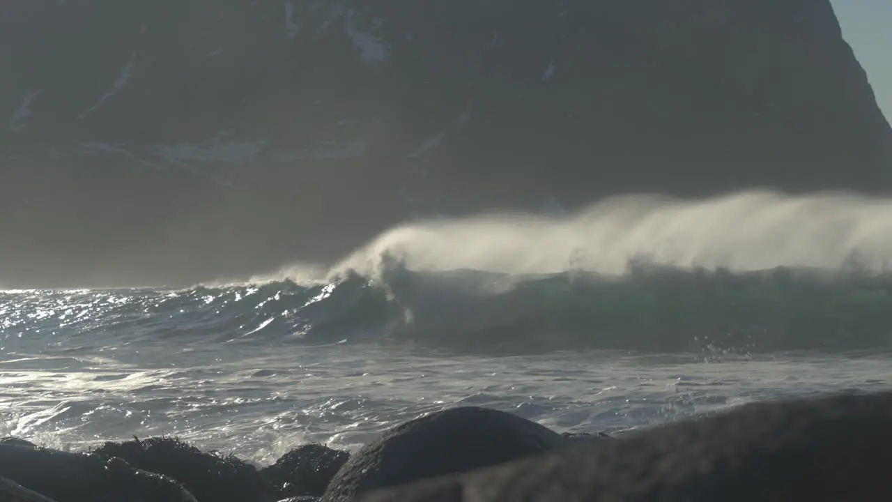 Waves break in slow motion on Unstad beach with a rugged mountain in the background