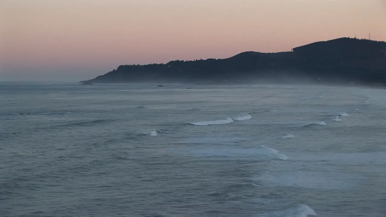 Mist Lies Above The Ocean Waves Rolling Towards Shore Beneath A Pastel Sky