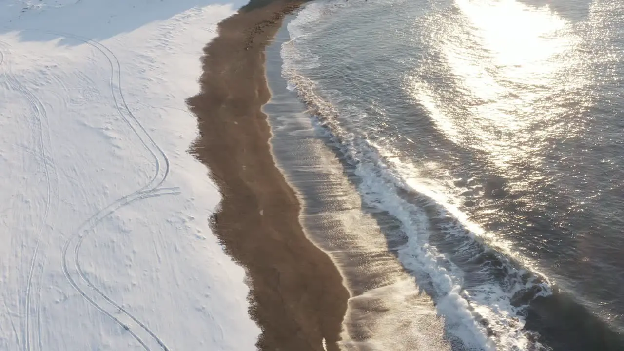 Midday sunlight shines bright on Sandvik beach covered in snow with waves