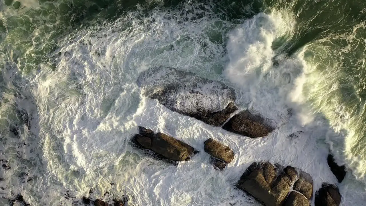 Mezmerizing Cinematic Cenital Gentle Rise Shot of Rough Ocean Waves Hitting Rocks During Sunset at Cape Town's Camps Bay Beach