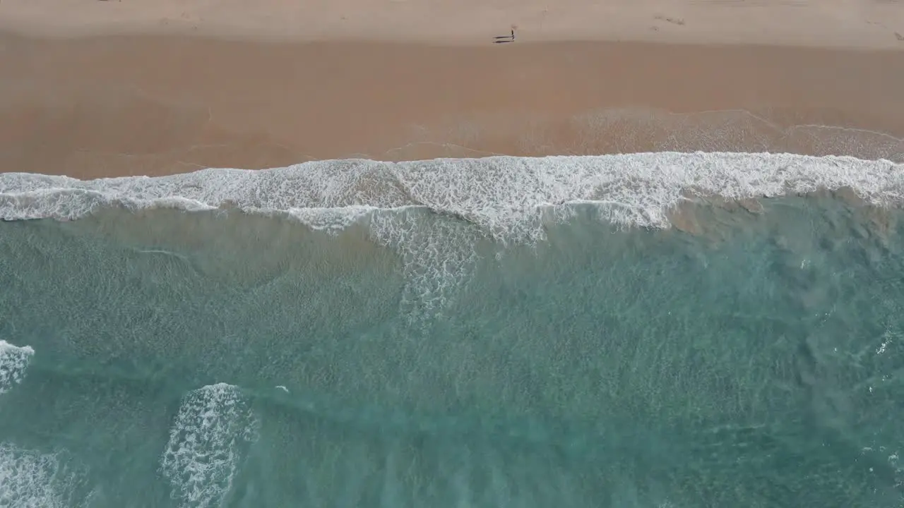 Aerial view over ocean surf to reveal waterfront hotels and wind turbines across mountain countryside