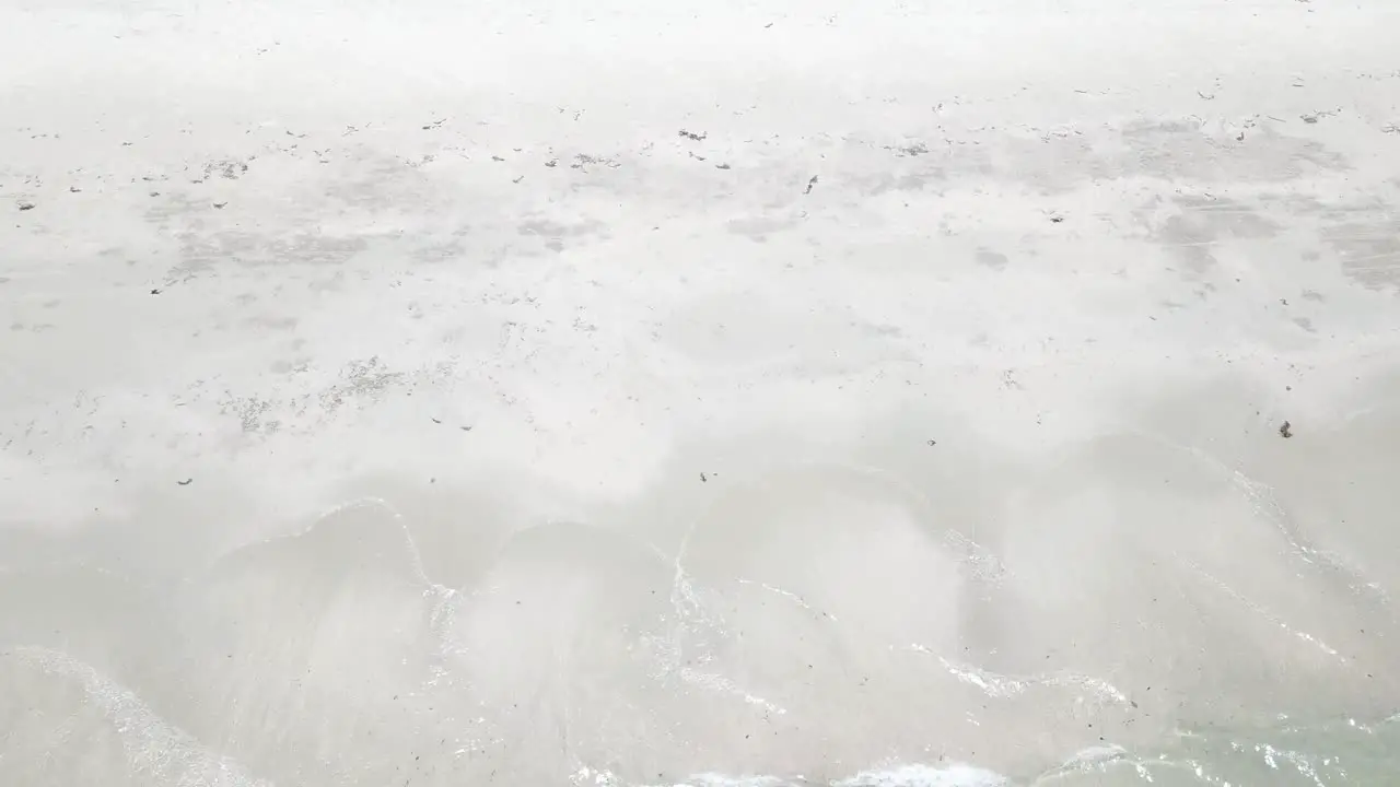 Drone aerial side ways over tropical blue water and then rise to reveal sand