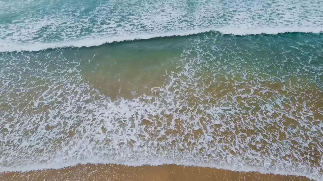 High angle shot of waves rolling into shore with white foam