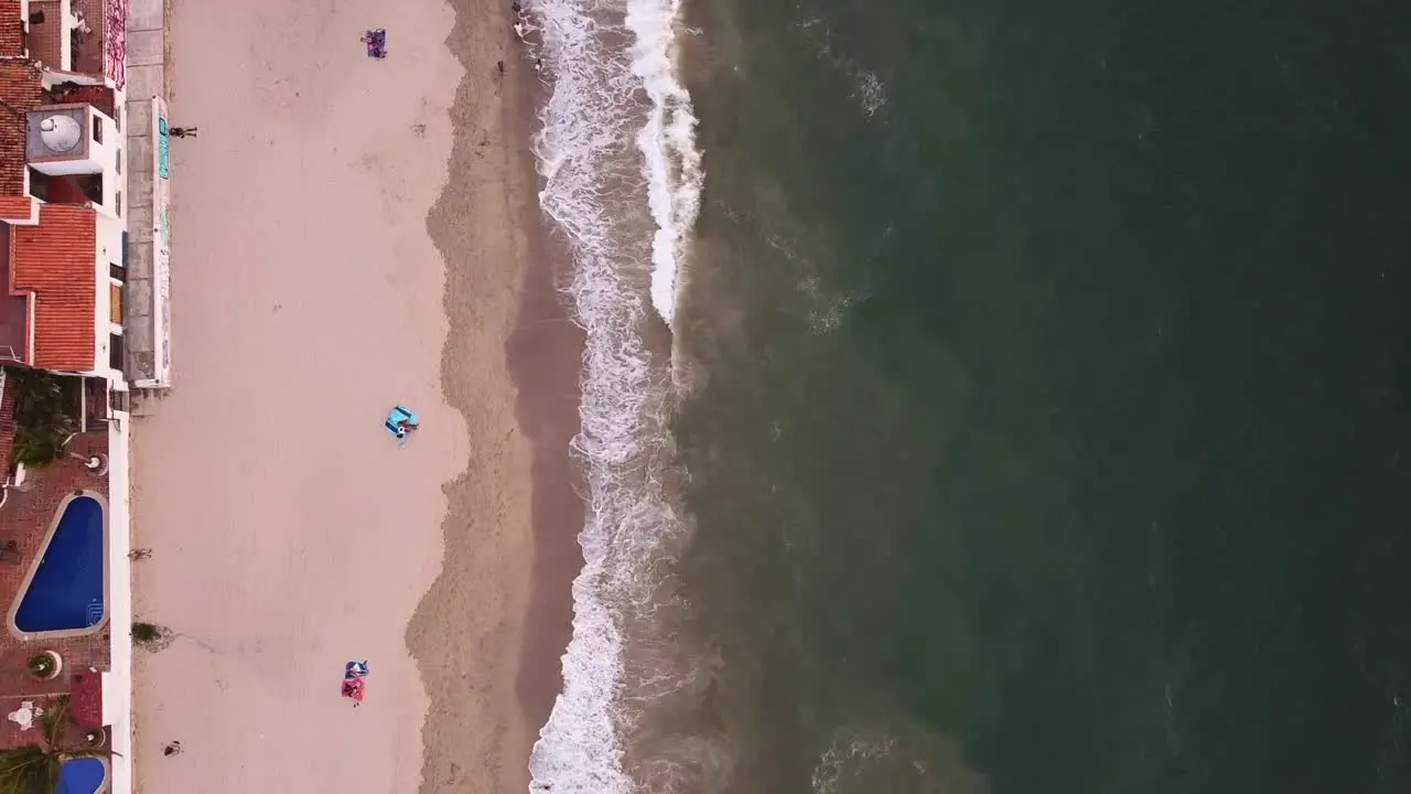 drone aerial view top down of relaxing view of green ocean waves crashing onto brown sandy Mexican beach in Puerto Vallarta at sunset