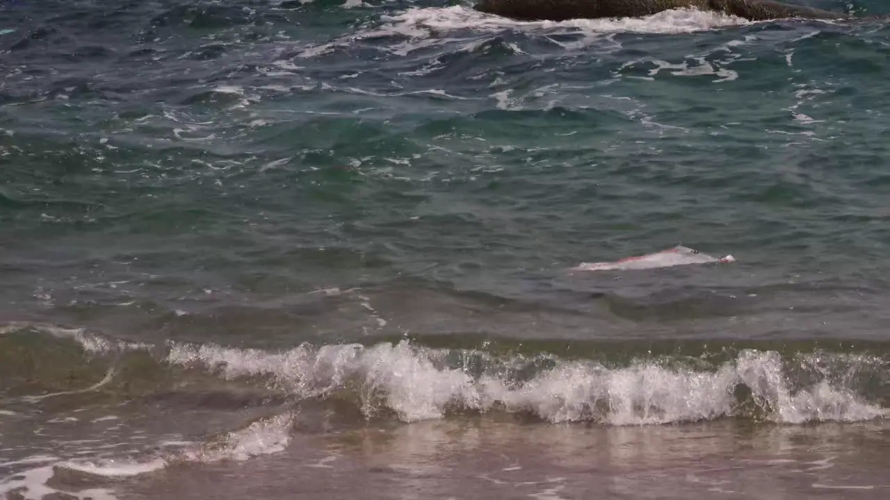 Rubbish bag drifting close to the beach with waves steady shoot 4K Asia Thailand Filmed with Sony AX700