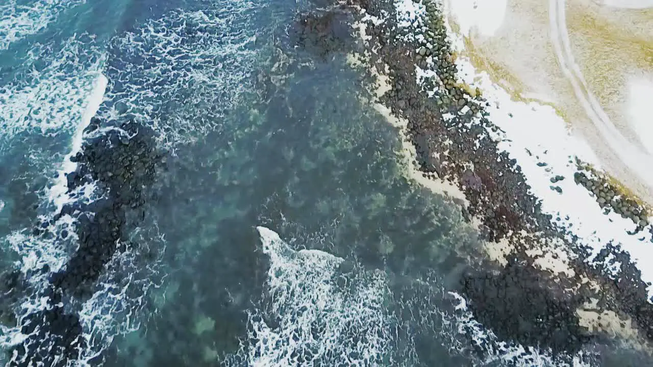 Aerial shot pointed down at Sandgerdi Iceland coast showing crashing white peaked waves and clear water with black rocks