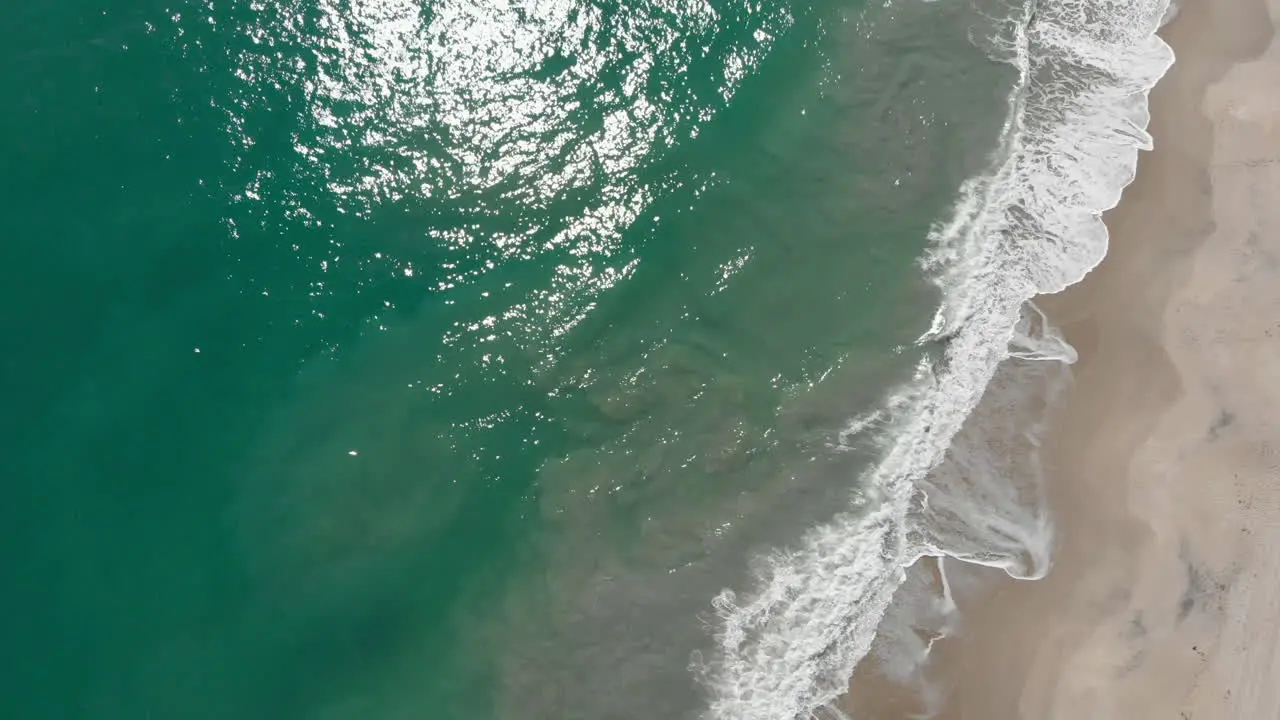 Aerial top-down shot flying along a beach with the waves rolling in during the afternoon