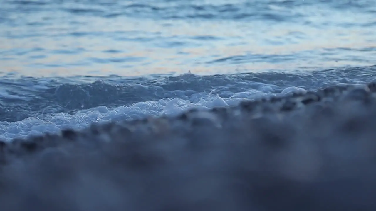 Sea water texture waves foaming on shore with pebbles at morning sunlight