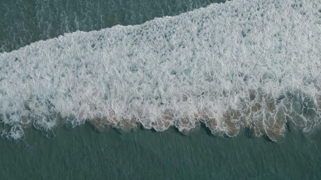 Turquoise foaming ocean breaking against sandy shore aerial top down view above surf