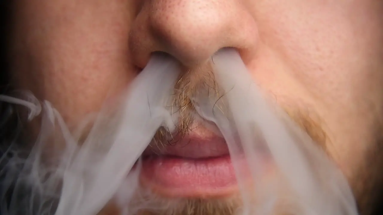 Man exhales vapor through his nose in slow motion