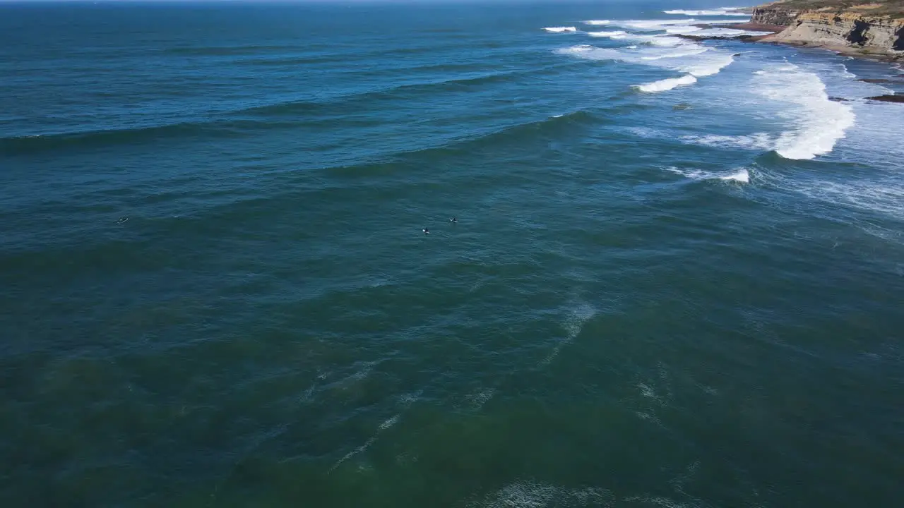 Aerial view of three surfers in the water waiting for the perfect waves in Ribeira de Ilhas Ericeira