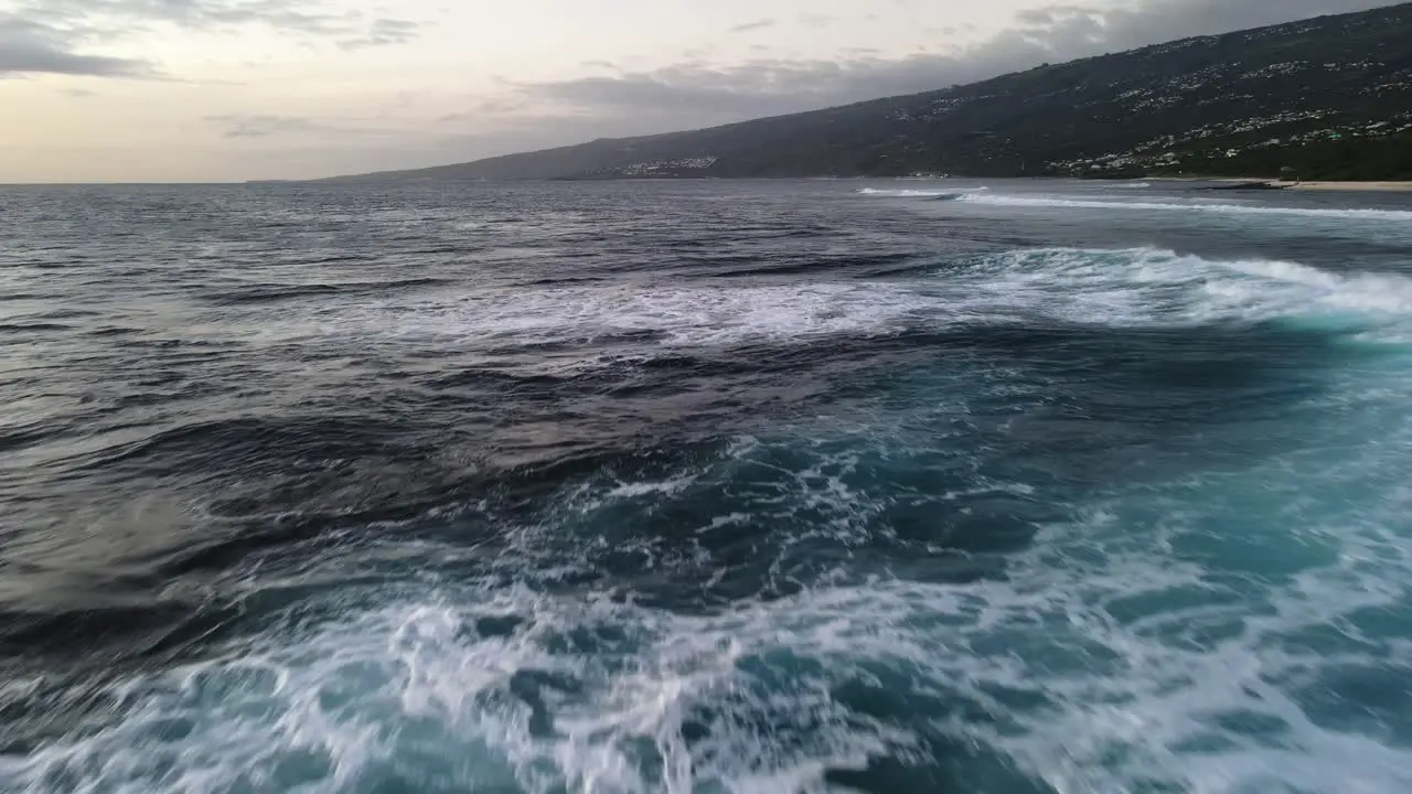 Close-up drone footage of waves crashing on a rocky beach made of cooled lava during sunset