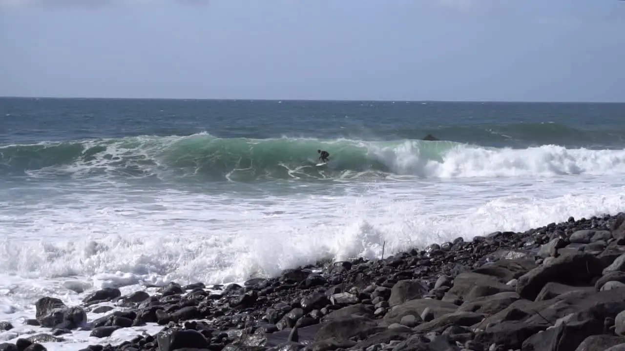 Slow Motion footage of a surfer getting a big wave at a rocky beach