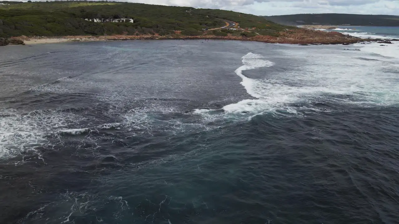 Aerial flight over ocean with waves rolling and cars driving along the coastal road