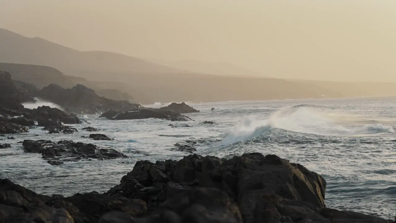 Rocky ocean shore with waves splashing on rocks and orange sky in the background