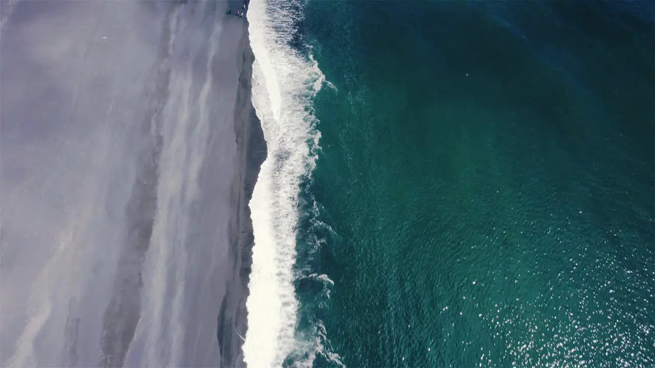 Drone shot flying over green sea and black beach shore with camera tilting up slowly in Iceland 4k