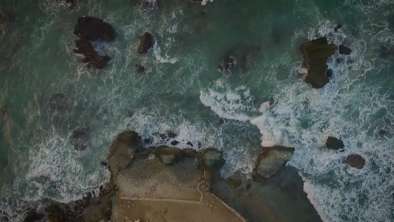 Cenital clip seeing several rocks being hitted by waves during a sunset on a rocky beach