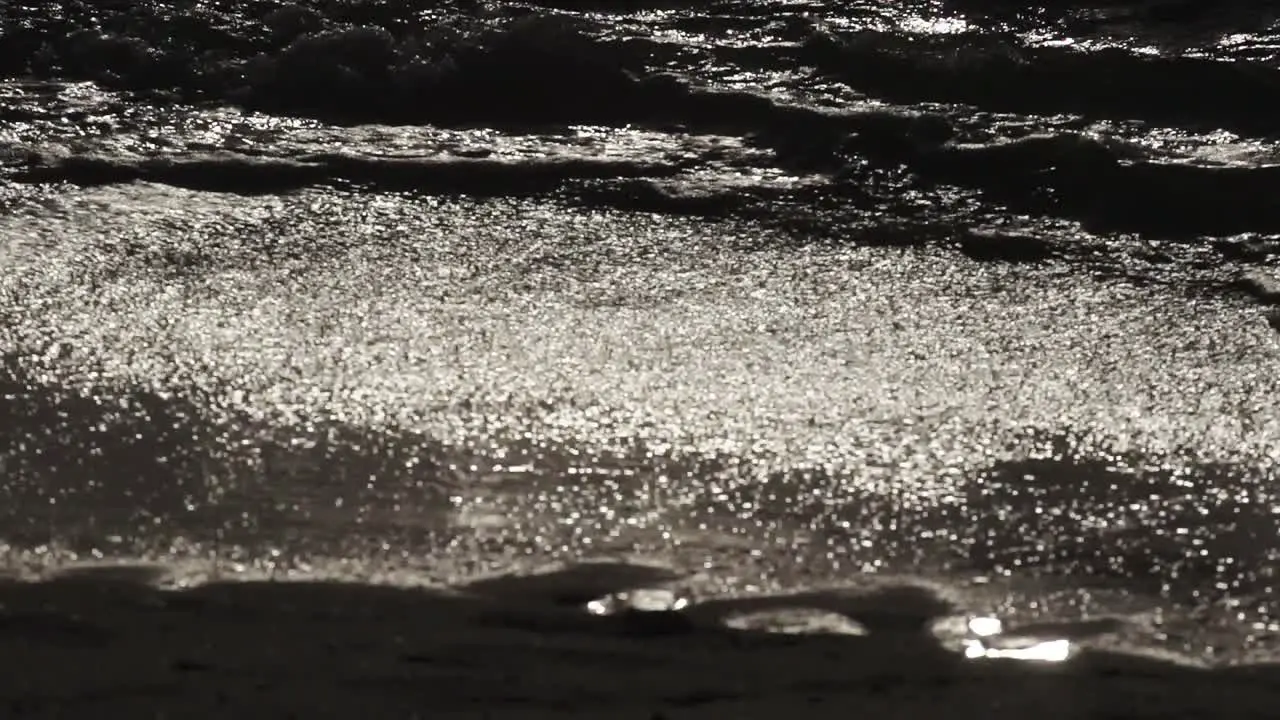 Slow motion waves lap on dark beach at night